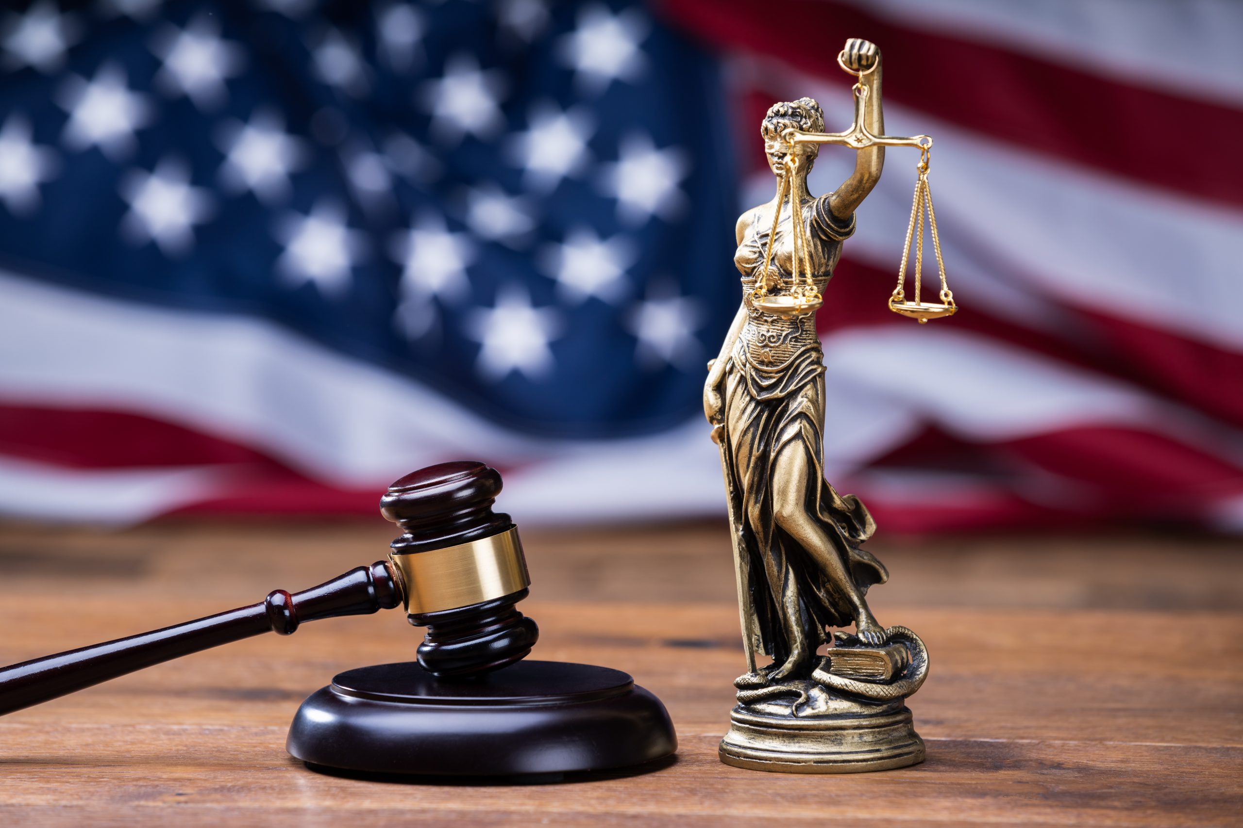 Statue of Lady Justice holding scales beside a gavel, with an American flag background, symbolizing legal representation and the impact of DWI on immigration status.